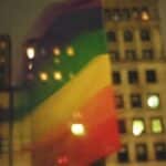 Vibrant LGBTQ+ pride flag waving against New York City's night skyline.