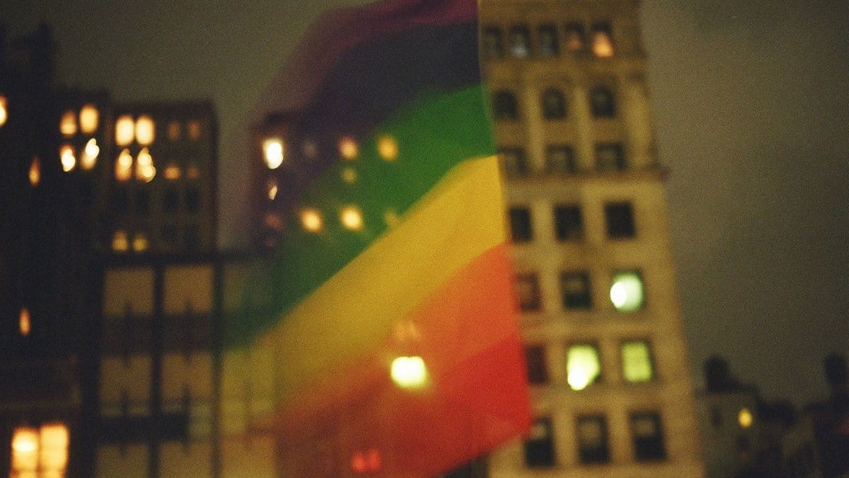 Vibrant LGBTQ+ pride flag waving against New York City's night skyline.