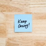 A blue sticky note with 'Keep Going!' message on wood background.