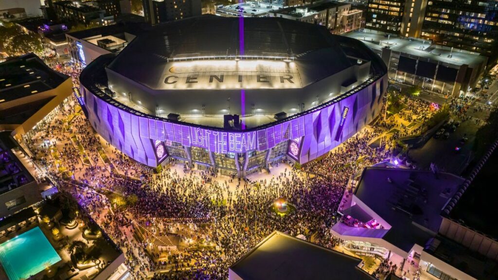 A vibrant night aerial view of Golden 1 Center in Sacramento, California during a lively event with a large crowd.