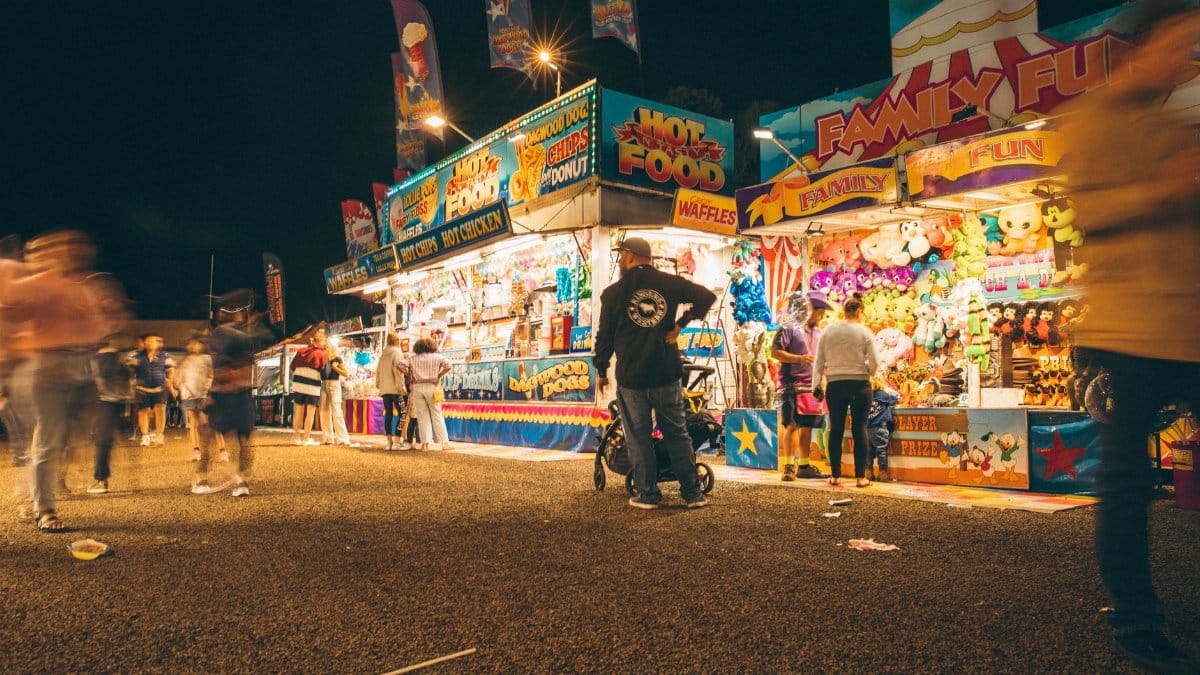 A lively night fair with illuminated stalls, games, and blurred motion of people.