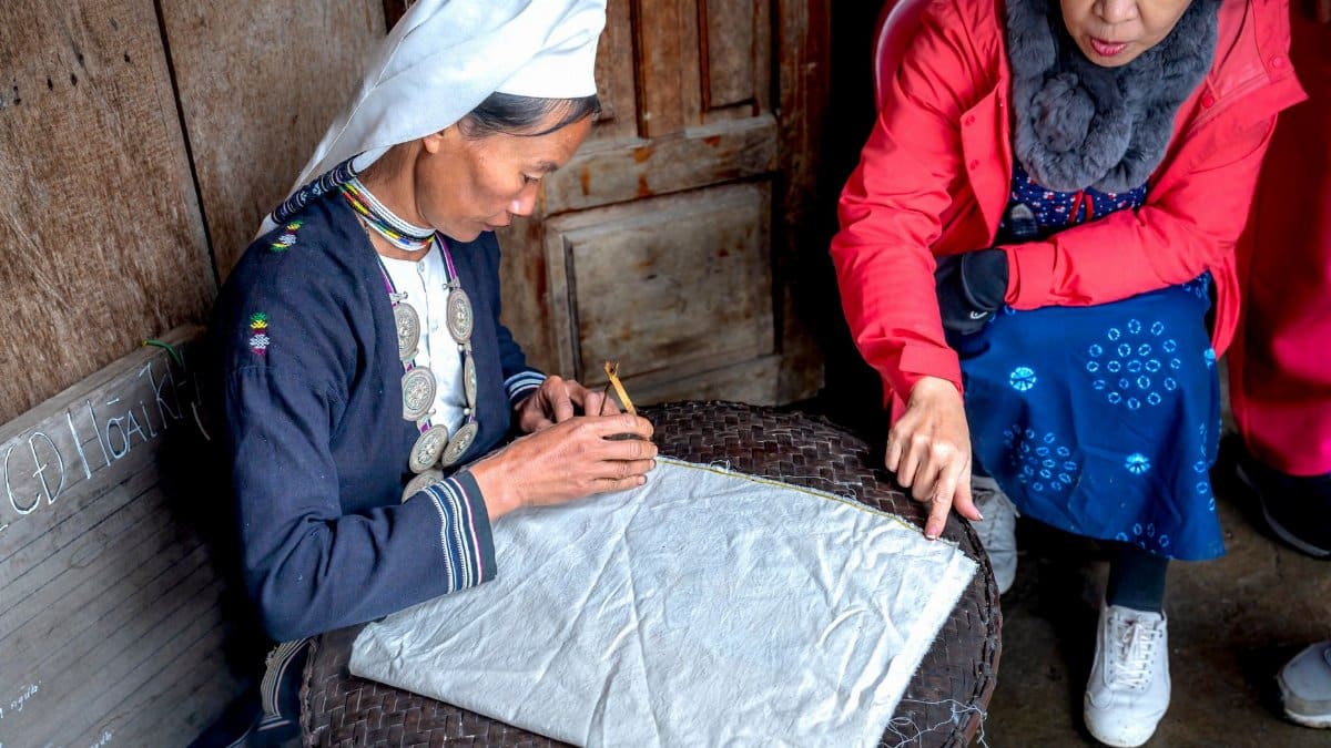 Elderly woman engaging in traditional textile crafting with guidance.
