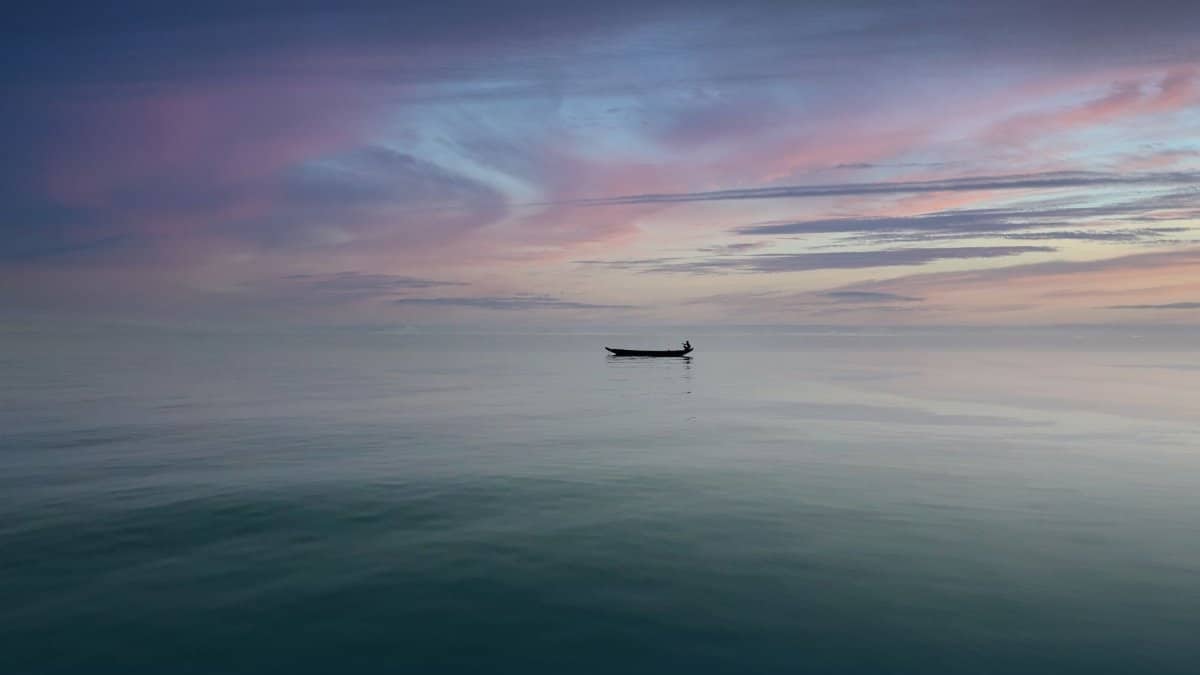 A lone boat at sunrise over a calm ocean with pastel skies in Bangladesh.