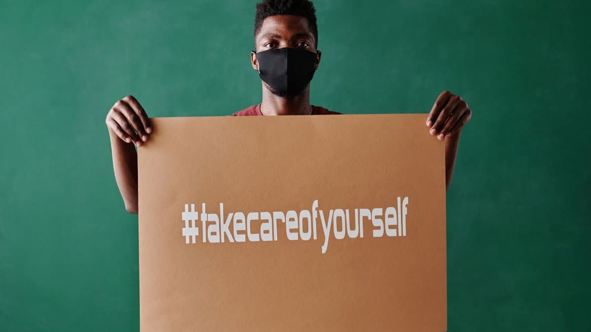 Person holding a self-care sign wearing a face mask, emphasizing mental health awareness.