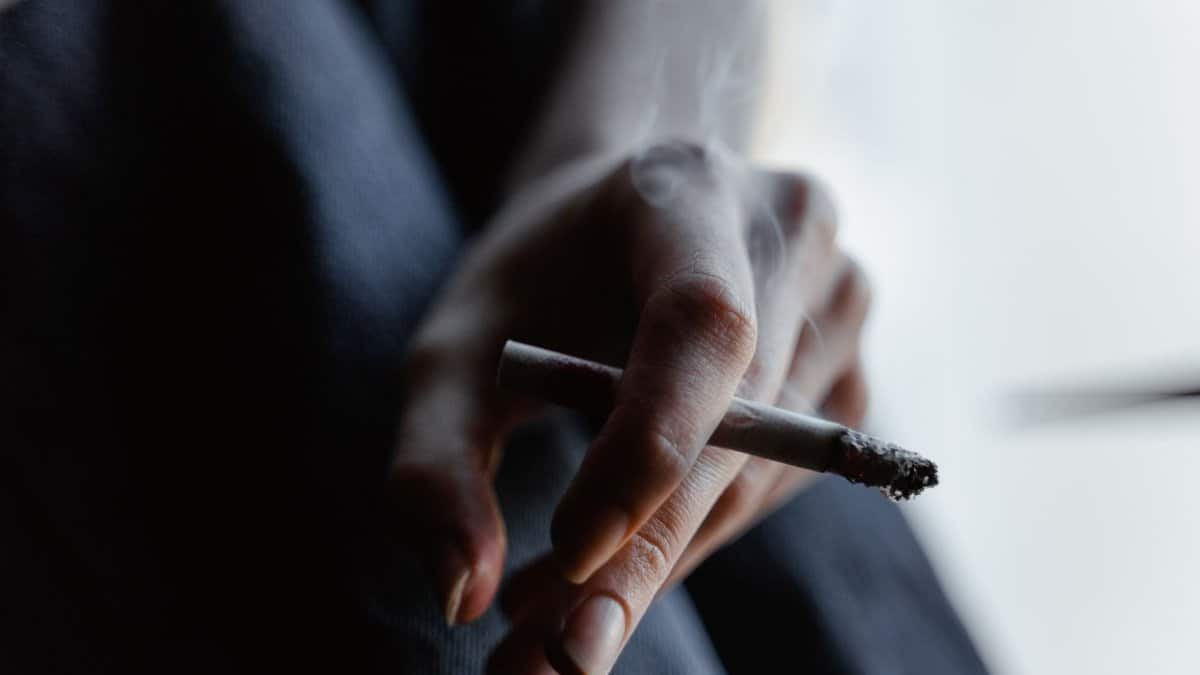 Moody close-up of a hand holding a burning cigarette indoors.