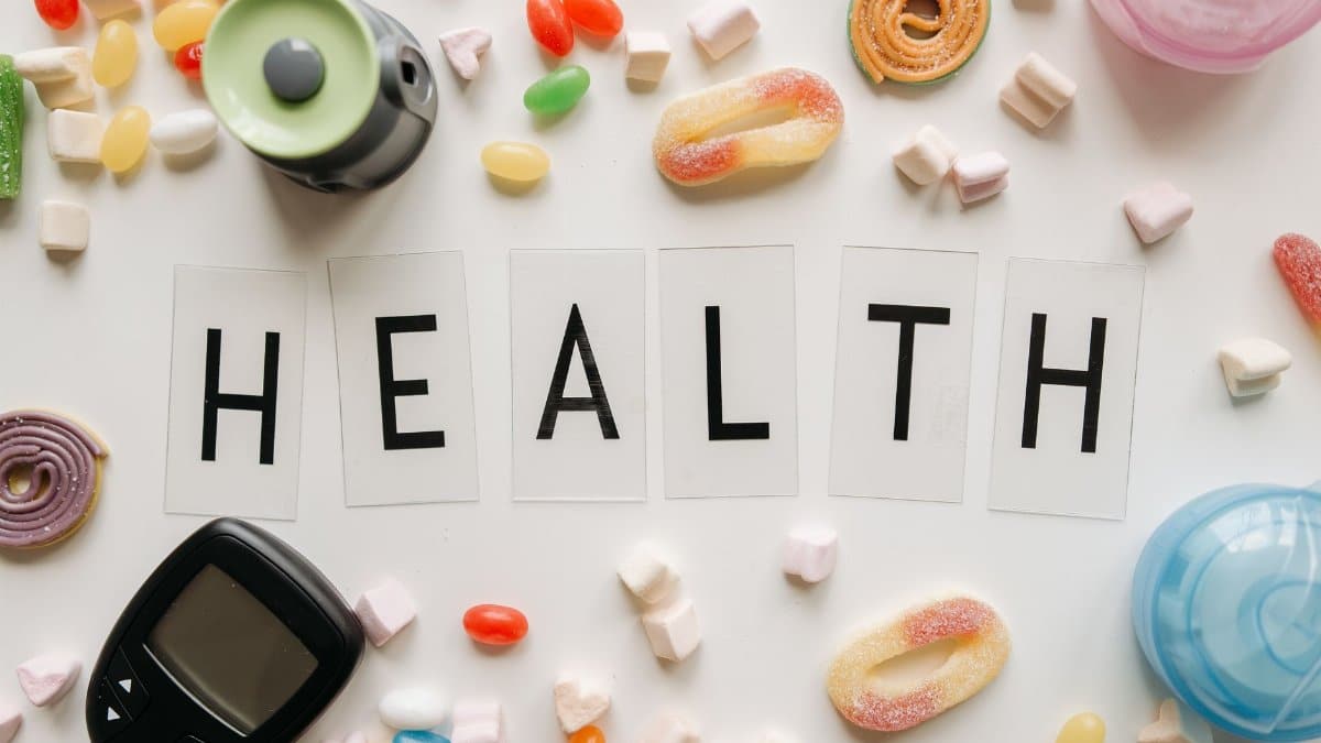 Creative flat lay with sweets around a 'HEALTH' text and monitoring device, symbolizing diabetes awareness.