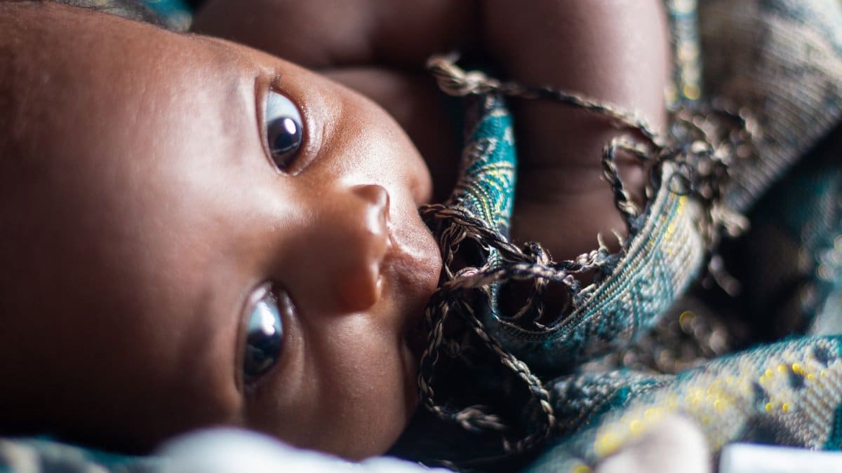 Adorable close-up portrait of a baby with expressive eyes wrapped in patterned fabric.