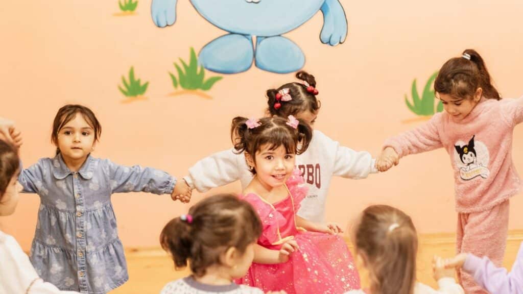 Happy children holding hands in a playful indoor circle game, enjoying a fun activity together.