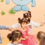 Happy children holding hands in a playful indoor circle game, enjoying a fun activity together.