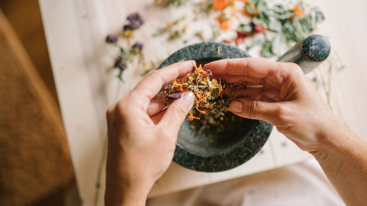 Close-up of hands preparing herbal ingredients in a mortar and pestle, top view.