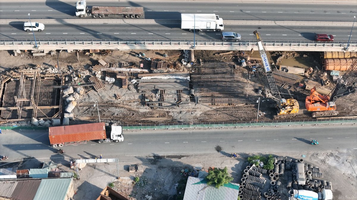 Aerial shot of a bridge construction site with vehicles passing on the highway above.