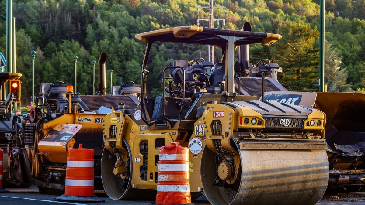 Construction machinery and vehicles on site with road rollers and cones.