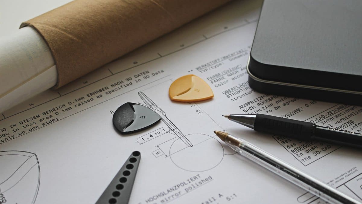 A technical engineering draft with guitar picks, pens, and a roll of paper showcasing precision and creativity.