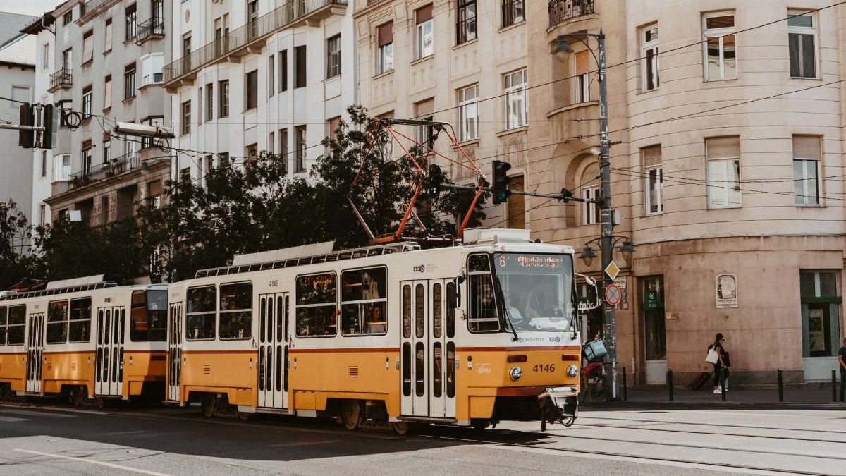 A classic yellow tram in Budapest travels along a city street, surrounded by historical buildings.