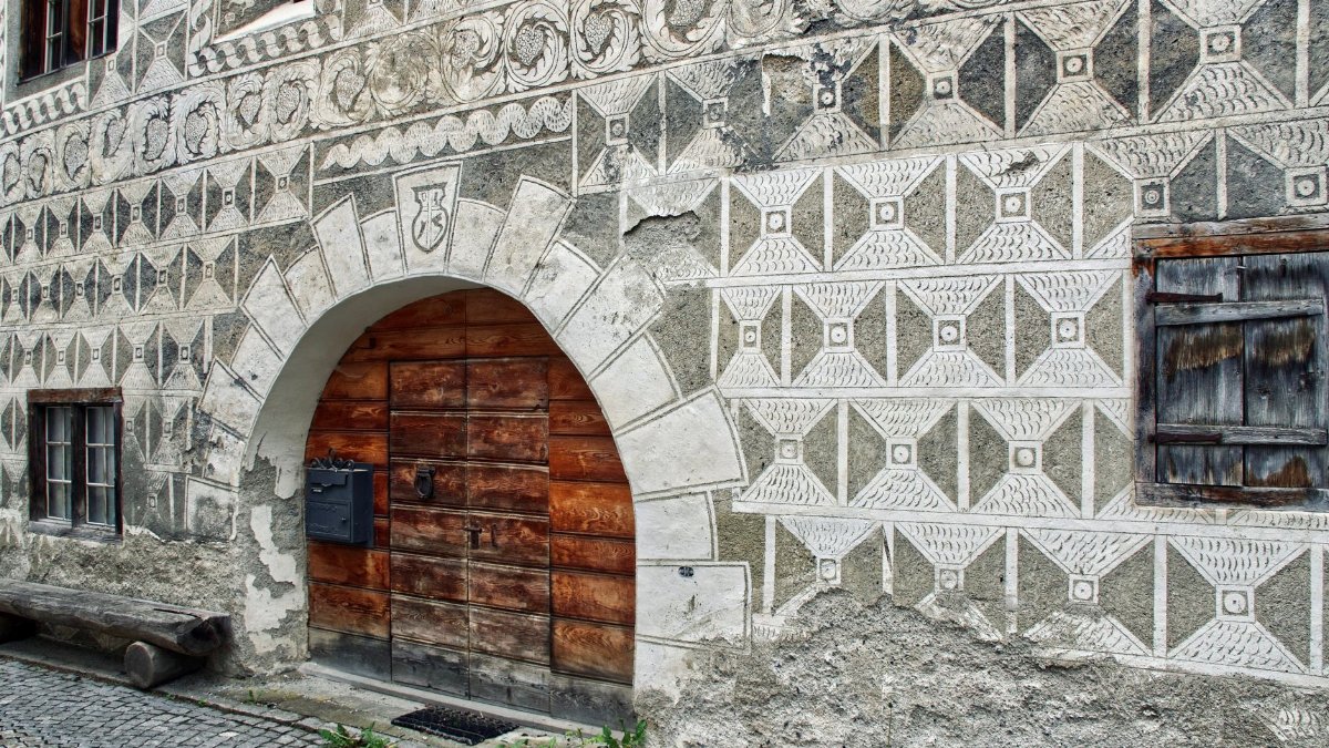 A close-up of a traditional Swiss stone building facade showcasing intricate geometric patterns and a wooden door.