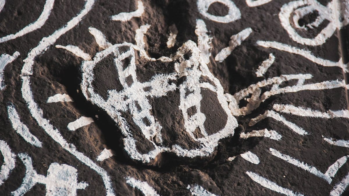Intricate white chalk patterns on a dark rock surface, artistic and historical.