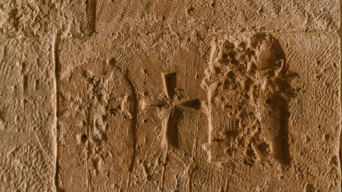Close-up of an ancient stone wall featuring intricate carving of a cross, highlighting historical texture.