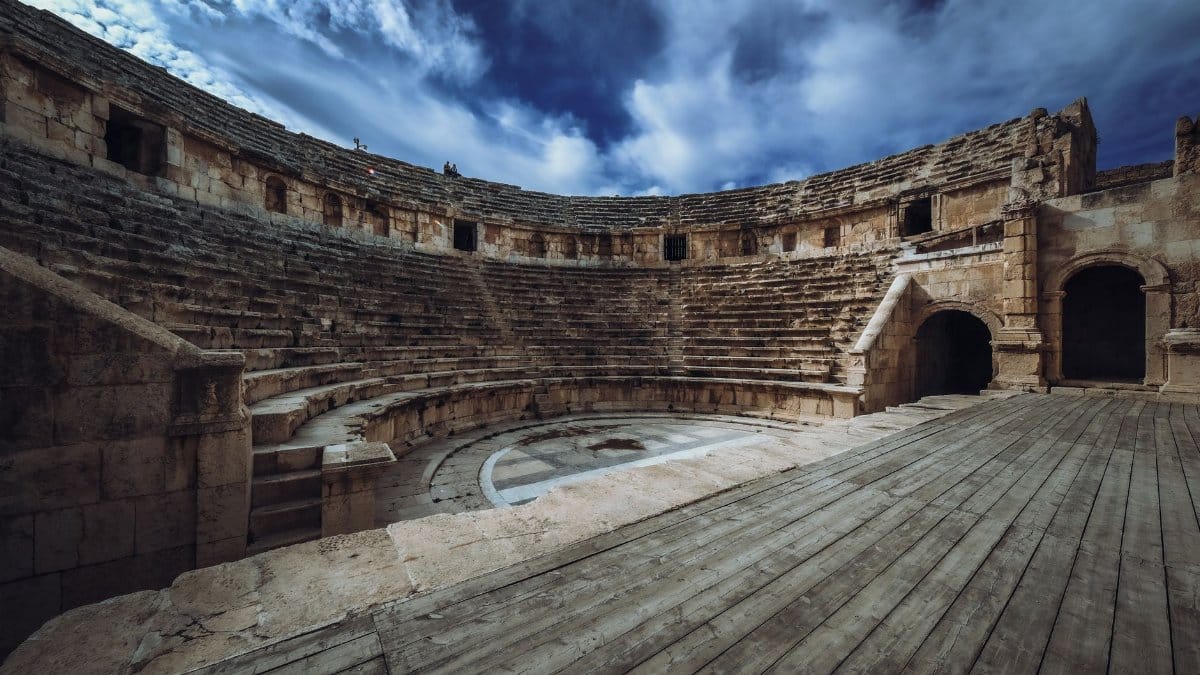Explore an ancient Roman amphitheater under a dramatic blue sky, showcasing historical architecture.