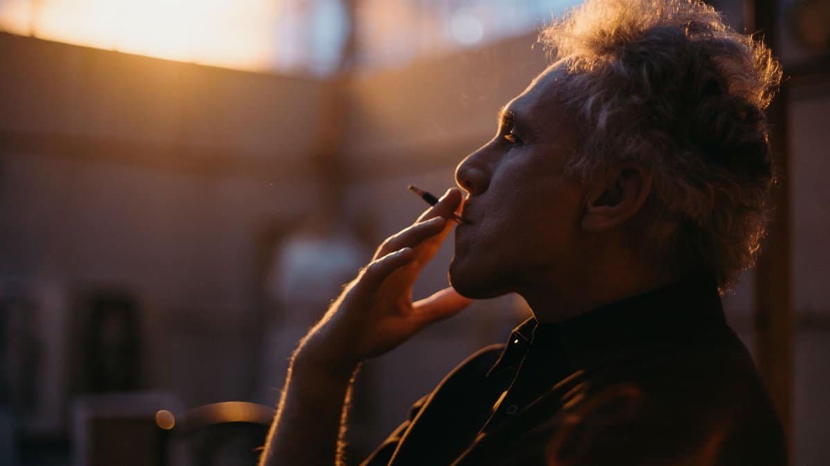 Side profile of man smoking indoors with warm sunset light.