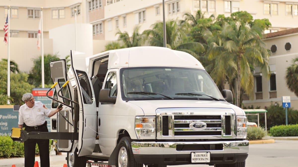 Van with wheelchair lift and driver assisting, located outdoors near a hospital or medical facility.