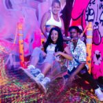 Vibrant neon-lit indoor party scene with friends enjoying a playful shopping cart ride amidst graffiti art.