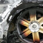 Detailed shot of a burned car wheel with rusty mag and damaged tire, showing fire aftermath.