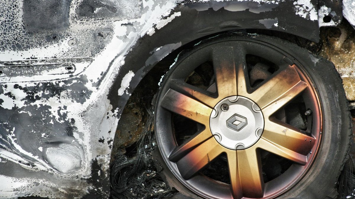 Detailed shot of a burned car wheel with rusty mag and damaged tire, showing fire aftermath.