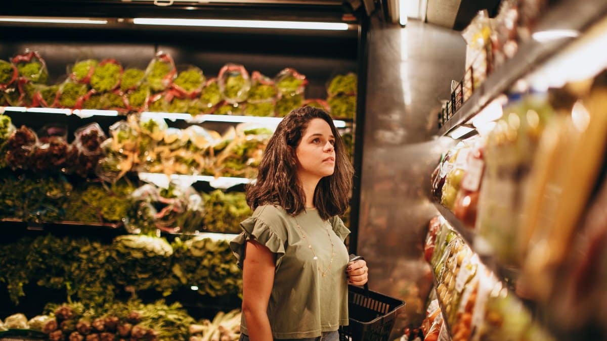 Woman browsing fresh produce with basket in supermarket. Indoor shopping scene.