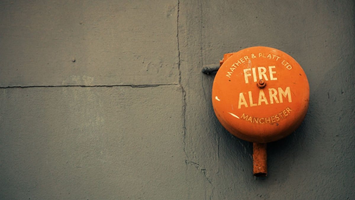 Close-up of an old fire alarm on a gray concrete wall, with text 'Mather & Platt Ltd Fire Alarm Manchester.'