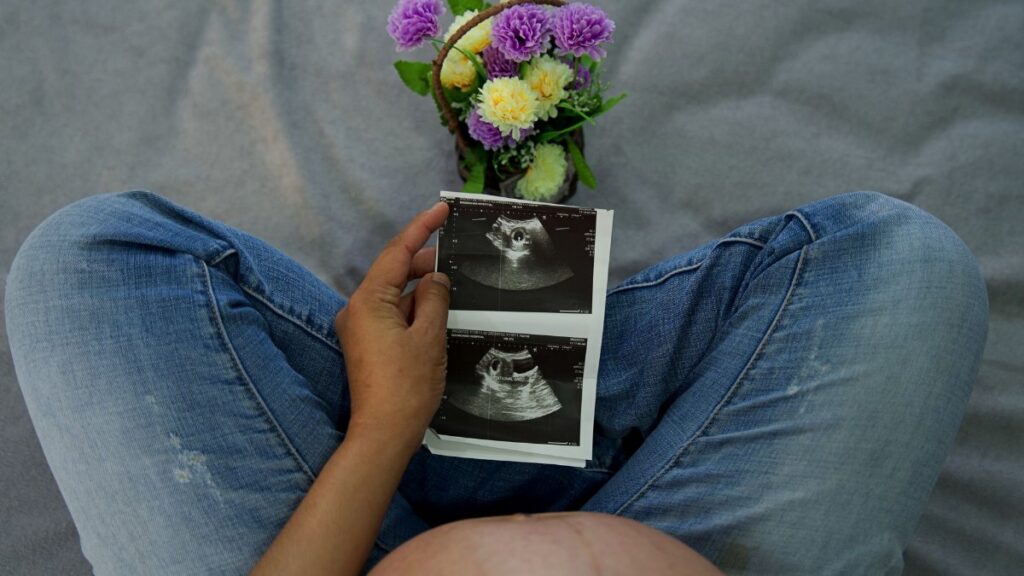 A pregnant woman holding ultrasound images with flowers, showcasing maternal joy.