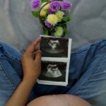A pregnant woman holding ultrasound images with flowers, showcasing maternal joy.