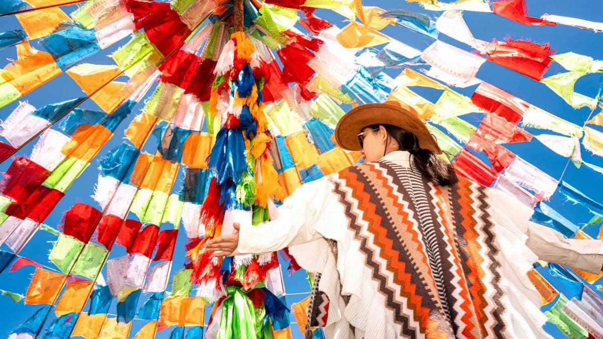 Person in traditional attire under a canopy of vibrant flags in Ulanqab, China.