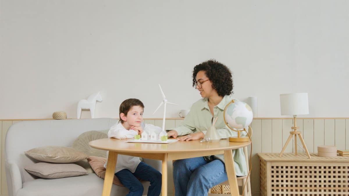 A woman teaches a boy about science with a globe and windmill model in a cozy home setting.
