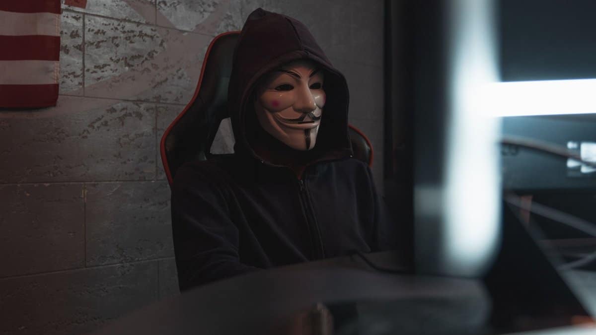 A mysterious person in a Guy Fawkes mask working at a computer, symbolizing cyber security themes.