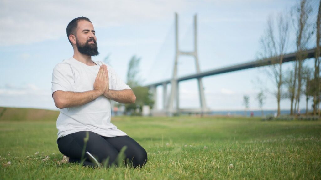 Man practicing meditation on green grass near a bridge in Portugal.