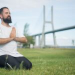 Man practicing meditation on green grass near a bridge in Portugal.