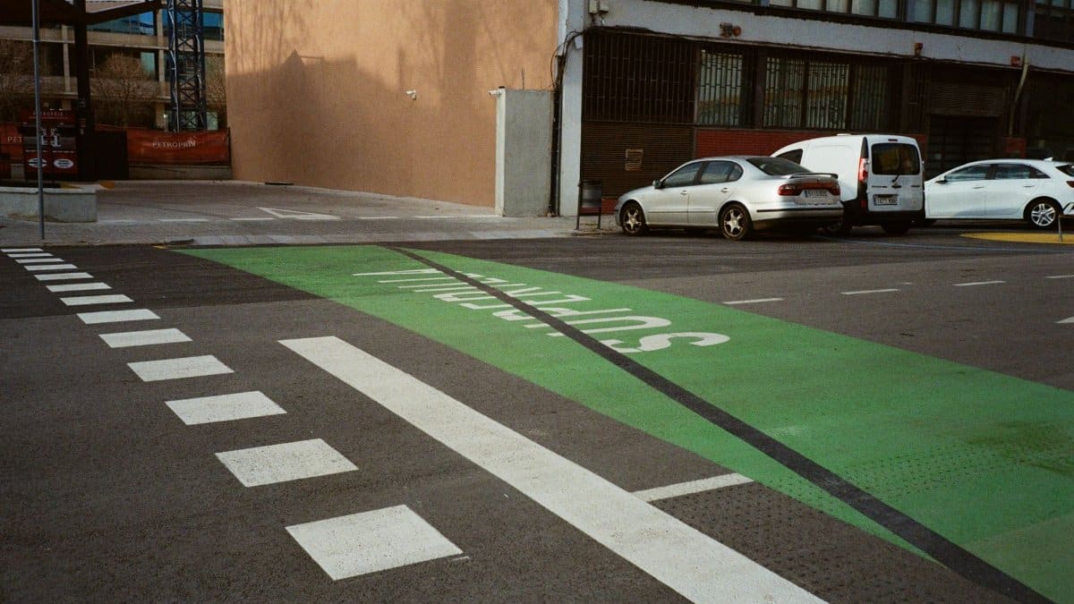 An urban street with parked cars and a marked green pedestrian lane.