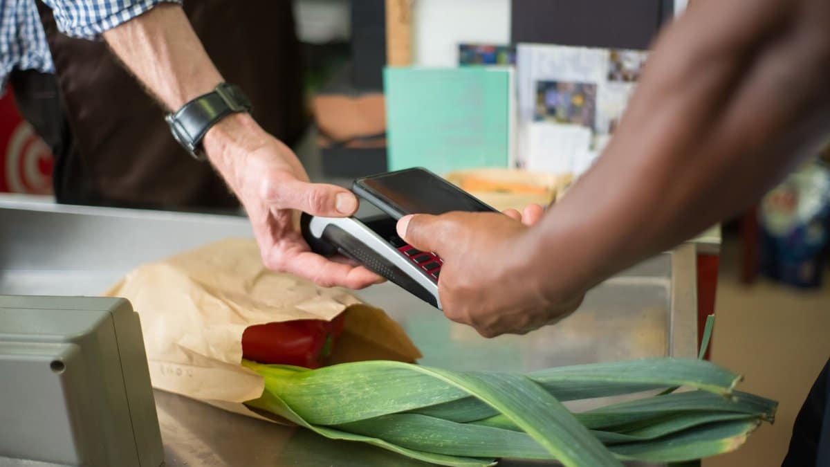 A customer making a contactless payment with a smartphone at a grocery store checkout counter.