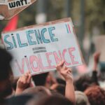 Anonymous person with poster Silence is Violence standing near board with stickers during peaceful Black Lives Matter protest