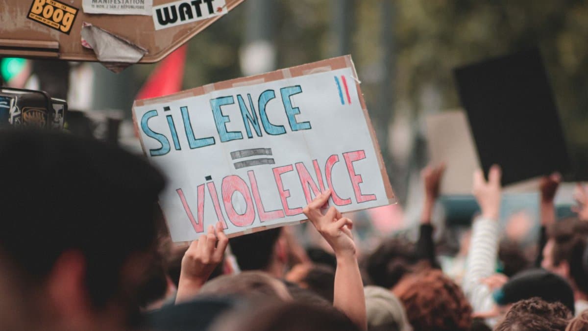 Anonymous person with poster Silence is Violence standing near board with stickers during peaceful Black Lives Matter protest