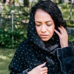 A woman in a cemetery expressing grief, wearing a polka dot headscarf, outdoors.