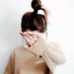 A woman in a sweatshirt raises her hand to cover her face, suggesting stop or privacy.
