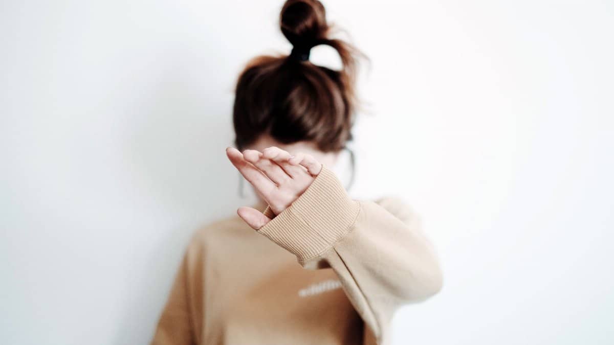 A woman in a sweatshirt raises her hand to cover her face, suggesting stop or privacy.
