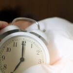 A close-up of a hand reaching for a ringing alarm clock, symbolizing waking up in the morning.
