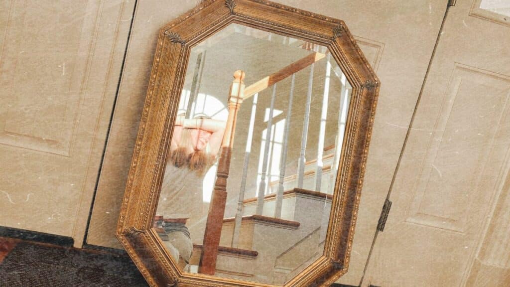 An ornate mirror reflects a cozy indoor staircase setting with warm tones.