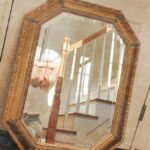 An ornate mirror reflects a cozy indoor staircase setting with warm tones.
