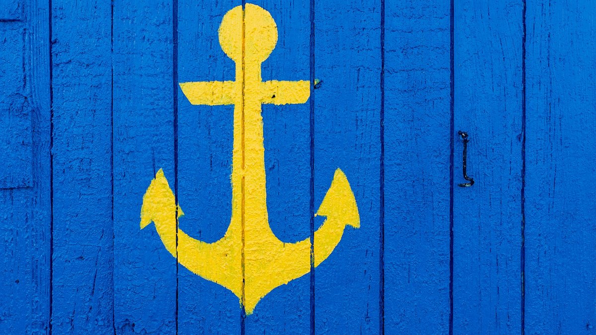Vibrant yellow anchor painted on a textured blue wooden surface, perfect for nautical themes.