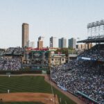 Crowded baseball stadium under a clear sky with cityscape background. Energetic game day atmosphere.