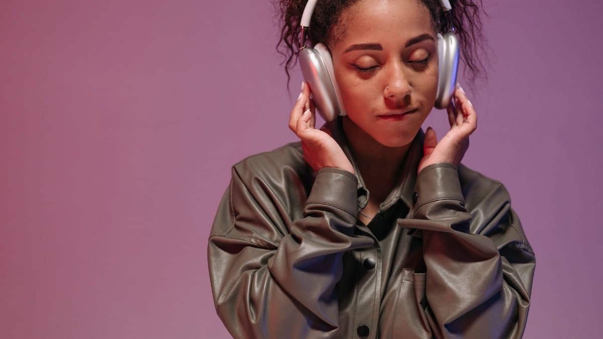 A woman in a gray leather jacket enjoys music with her eyes closed and headphones.
