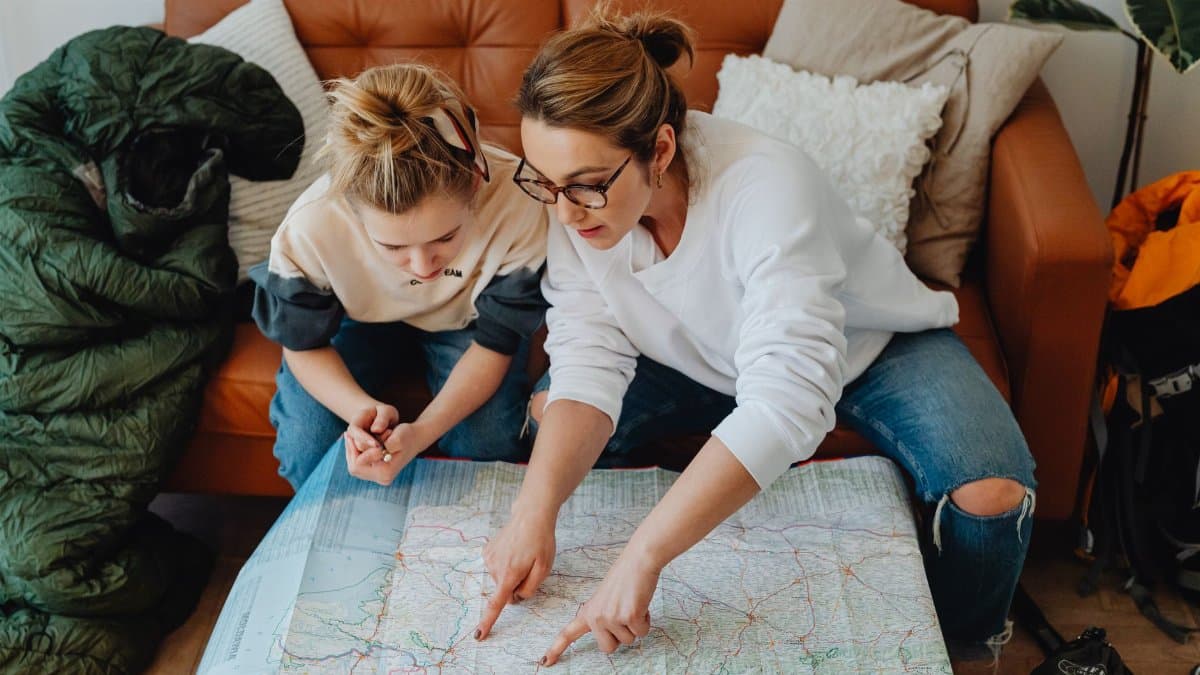 A mother and daughter discussing travel plans using a large paper map on the sofa.